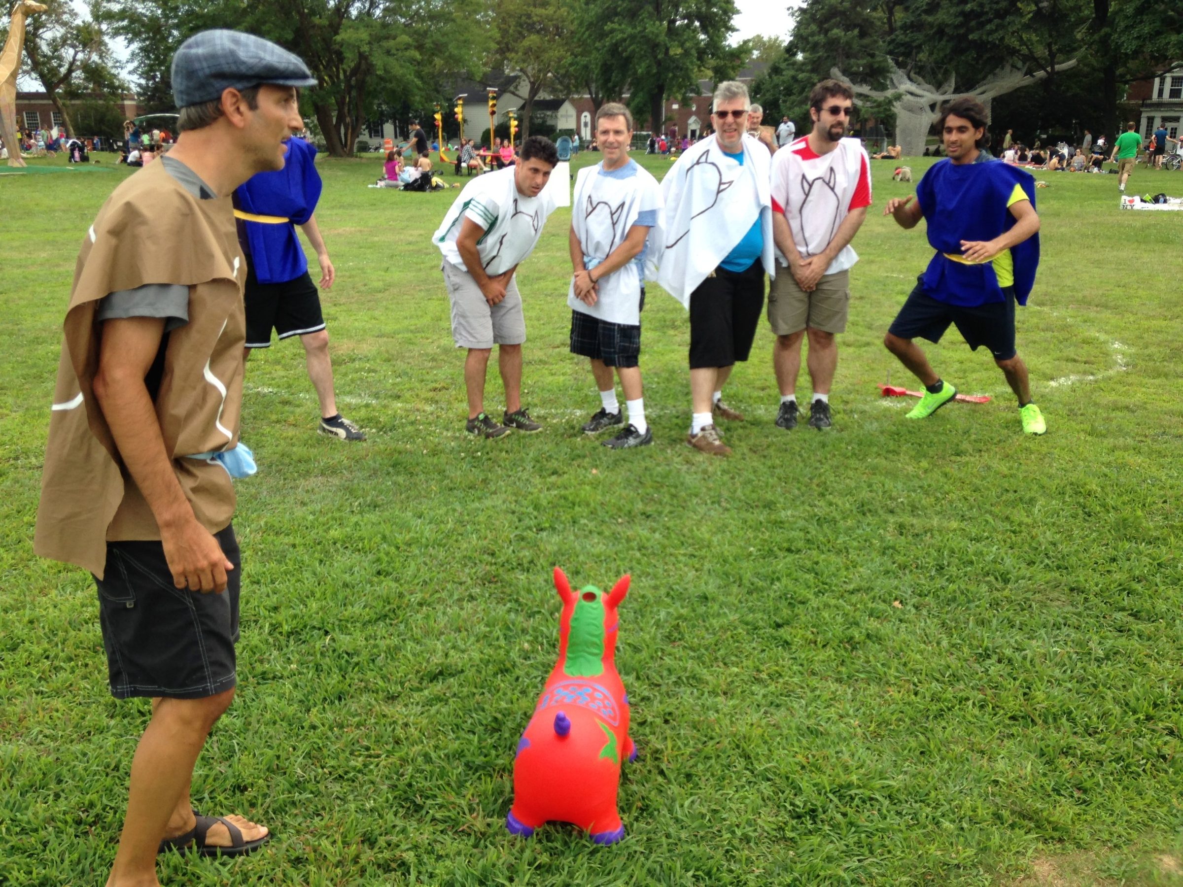 Players in paper tunics and white bibs with horse drawings stand on a lawn around an orange inflatable bouncing horse toy